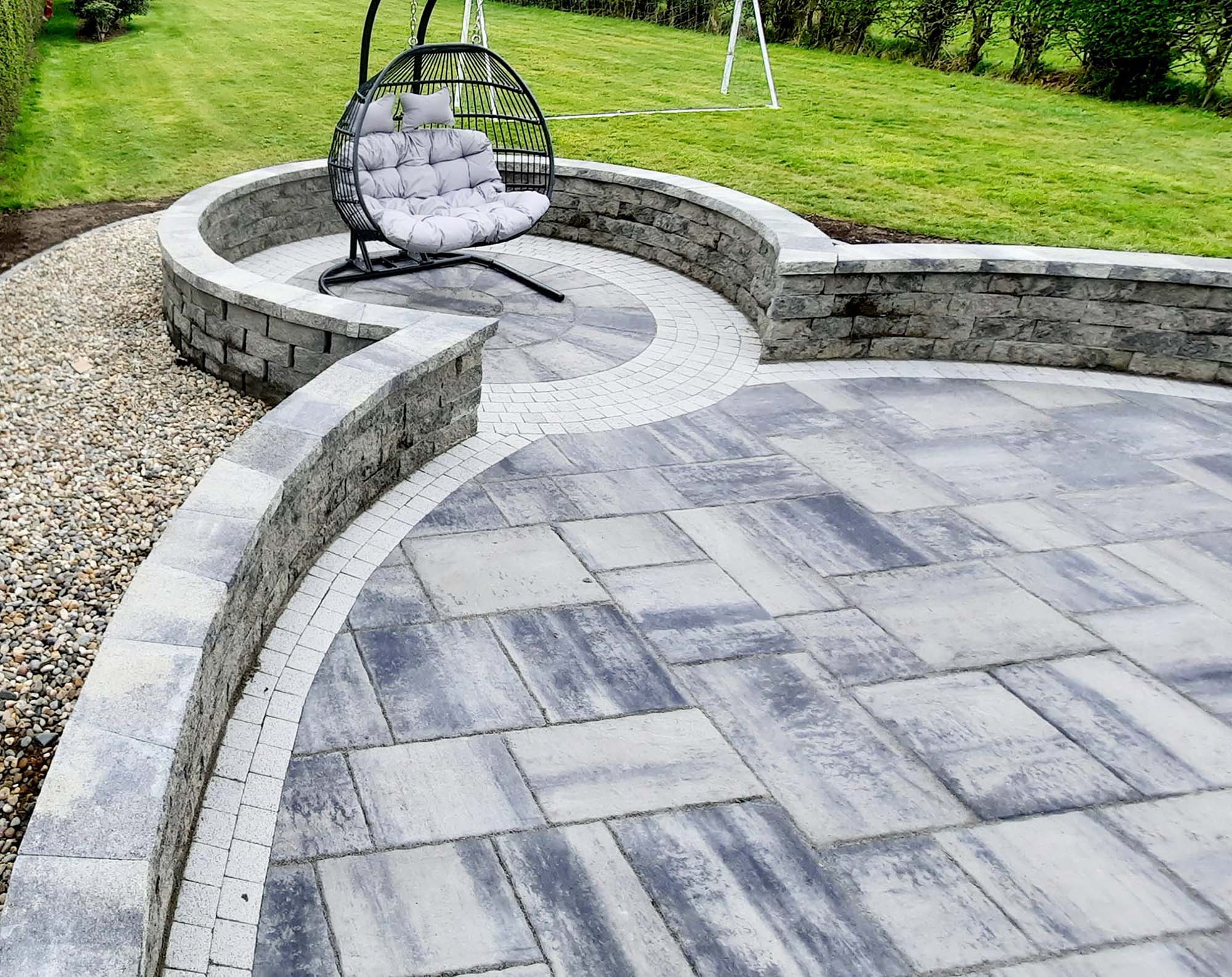 Circular patio with a stone border and a swinging chair in the middle